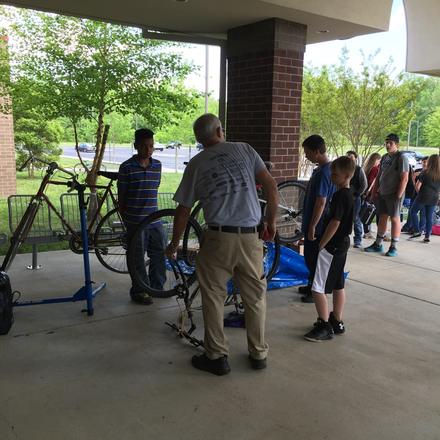 Volunteers and students working on bikes in repair stands under the school&rsquo;s covered walkway
